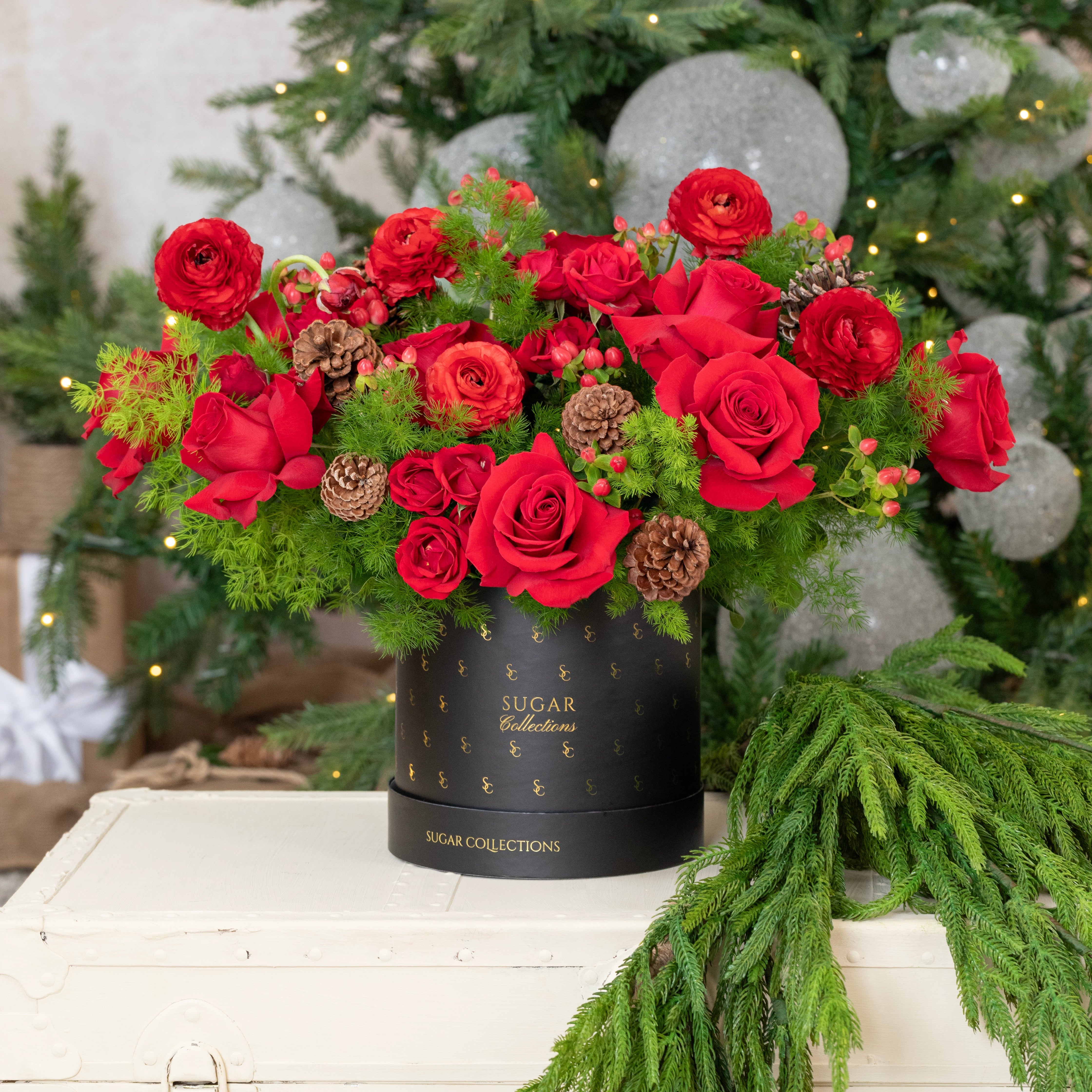 Bouquet of red roses in a black container with a Christmas tree in the background